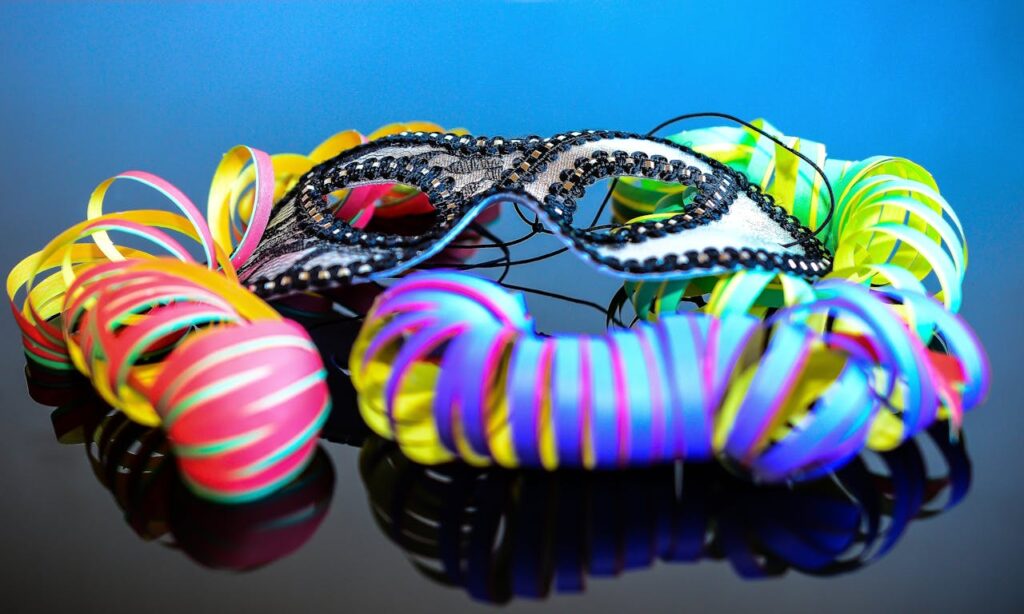 A vibrant close-up of a decorative mask surrounded by colorful streamers on a reflective surface.